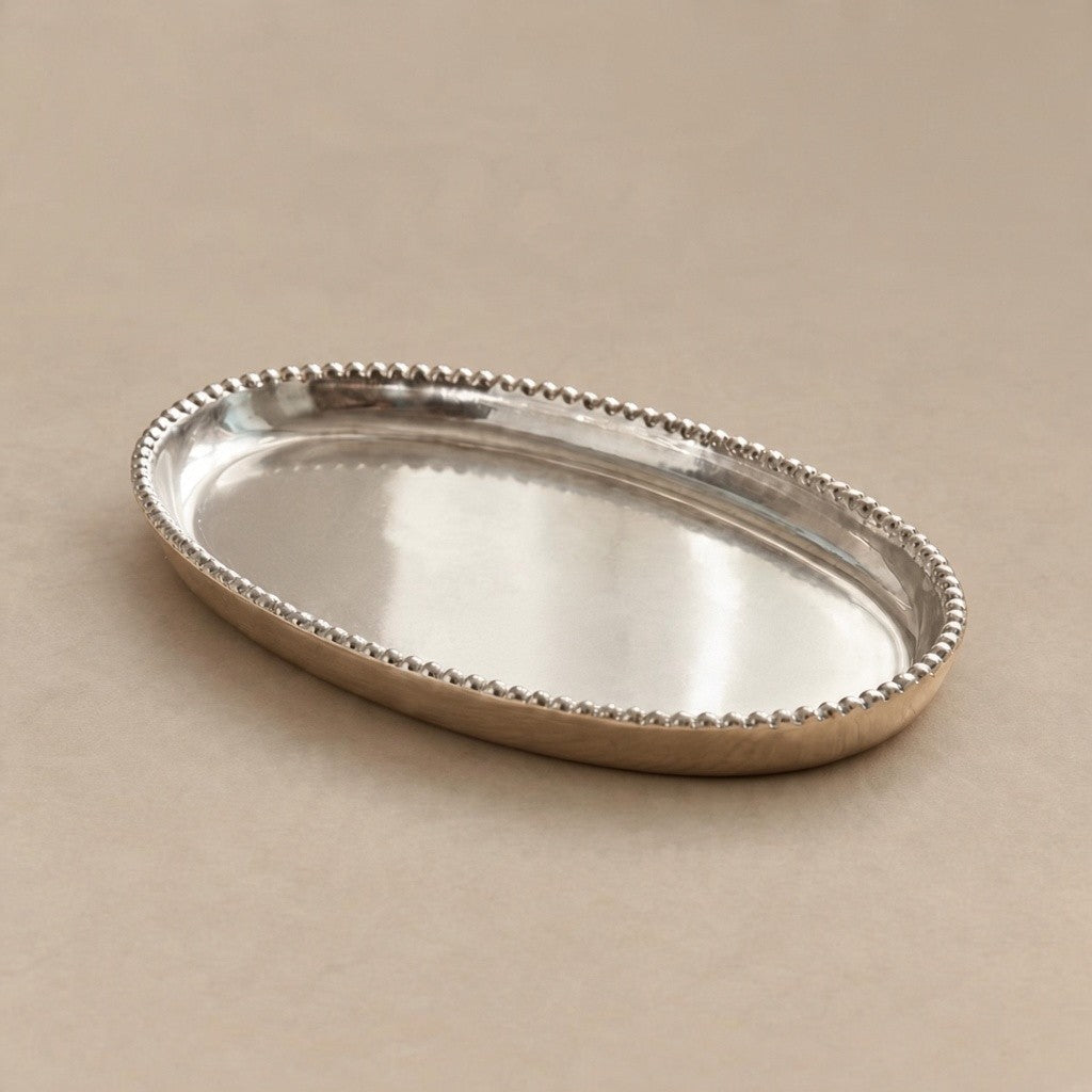An oval silver tray with a beaded edge, shown on a neutral beige background.