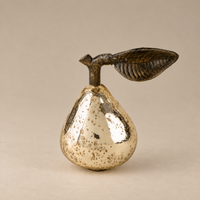 A decorative pear-shaped object with a metallic silver body speckled with gold, topped with a dark brown leaf and stem, set against a plain beige background.