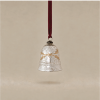 A hammered silver bell Christmas ornament with a gold wreath design, hanging from a dark red ribbon against a warm beige background.
