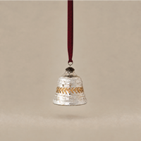 A hammered silver bell-shaped hanging ornament with a gold chevron pattern band and a dark red hanging ribbon, shown against a solid beige background.