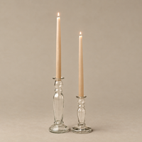 Two lit taper candles in clear glass candlestick holders on a warm beige background.
