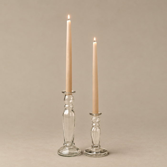 Two lit taper candles in clear glass candlestick holders on a warm beige background.