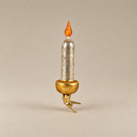 A miniature decorative candle-shaped ornament with a textured silver body, a gold-colored base, and an orange flame tip, set against a solid neutral beige background.