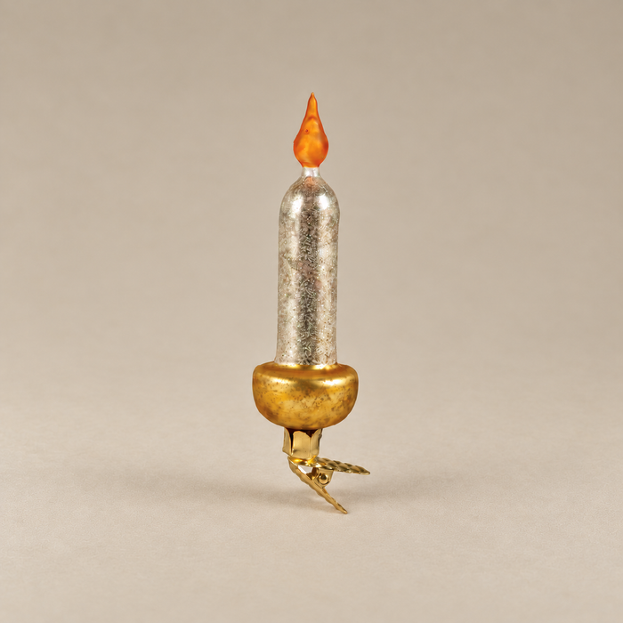 A miniature decorative candle-shaped ornament with a textured silver body, a gold-colored base, and an orange flame tip, set against a solid neutral beige background.