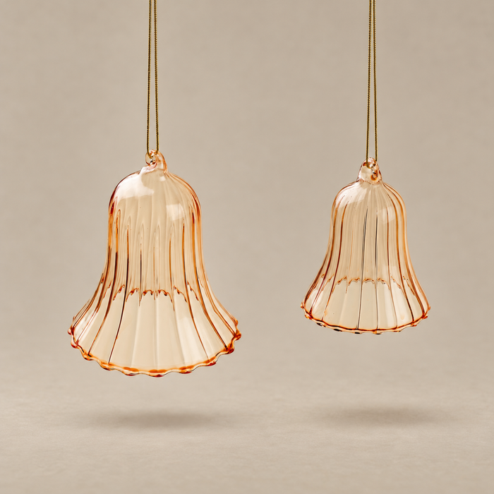 Two amber-tinted glass bell-shaped hanging ornaments with ribbed flared edges, suspended by thin cords against a warm beige background.