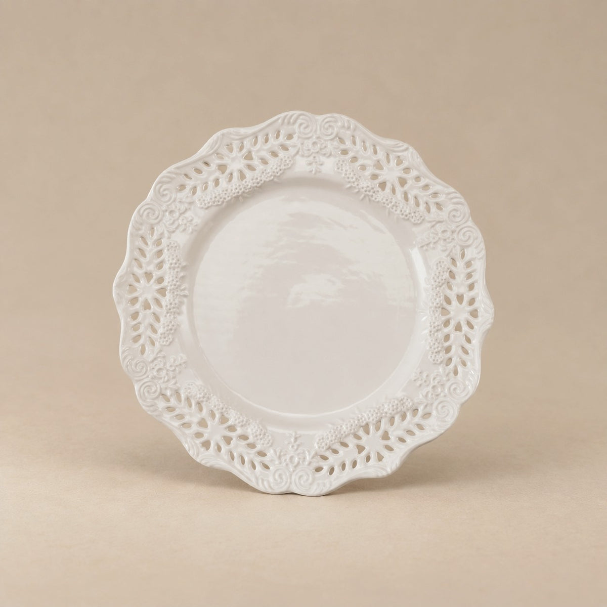 A white ceramic plate with an intricate, scalloped floral lace border, photographed against a solid beige background.