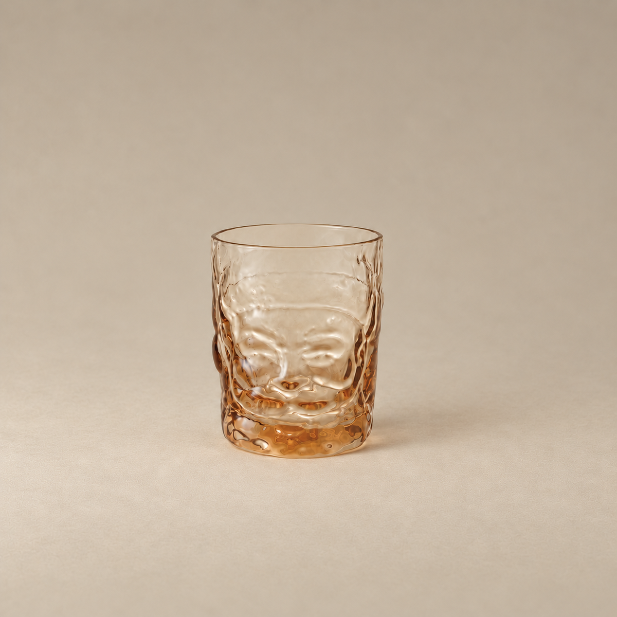 A textured clear glass tumbler with a warm amber tint, featuring a raised face design on the front, set against a solid neutral beige background.