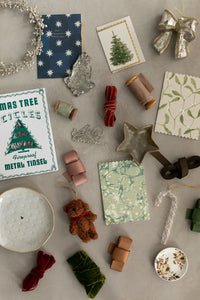 Collection of Christmas-themed items including tinsel, cards, and decorations on a textured surface.