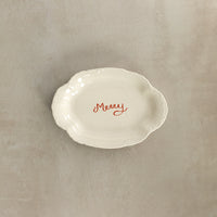 White ceramic dish with 'Merry' text on a beige background